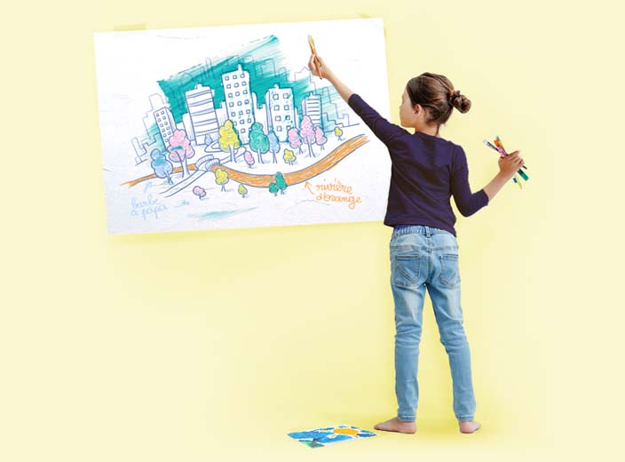 A girl decorating a wall with a painting of a city