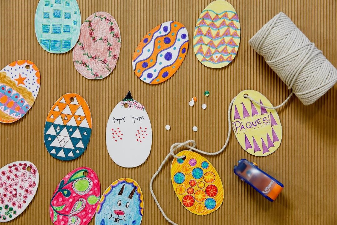 Decorated paper eggs laying next to string and a hole punch