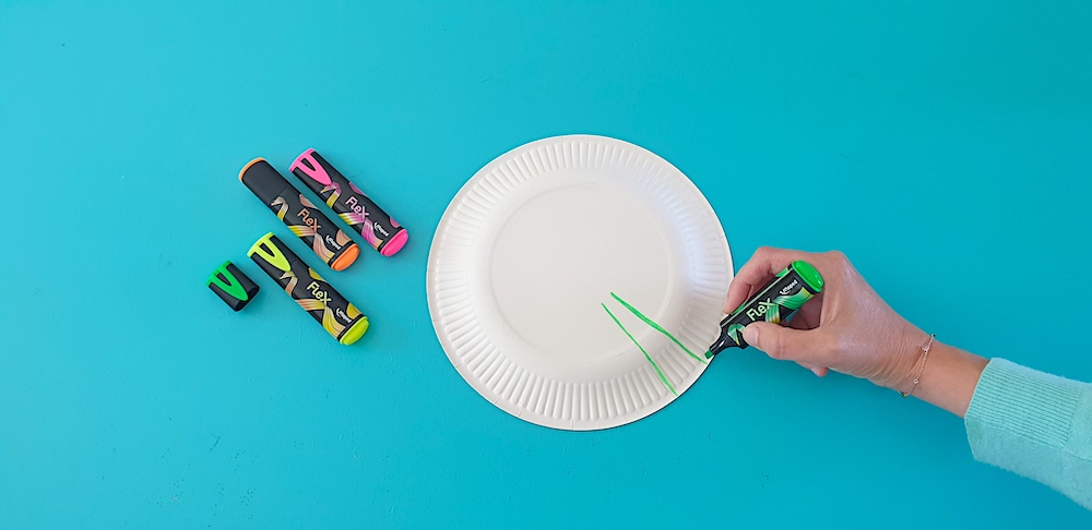 A hand decorating a paper plate with highlighters