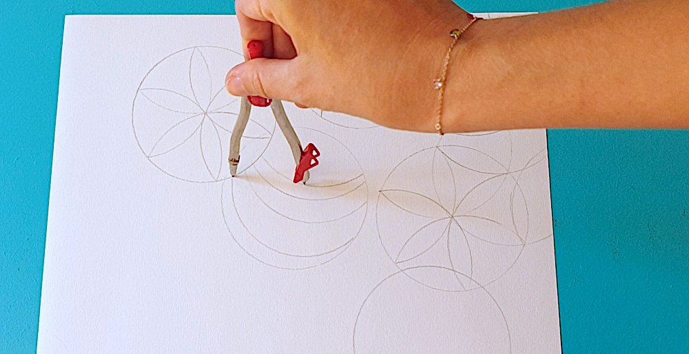 A hand holding a compass drawing a pattern on a white piece of paper