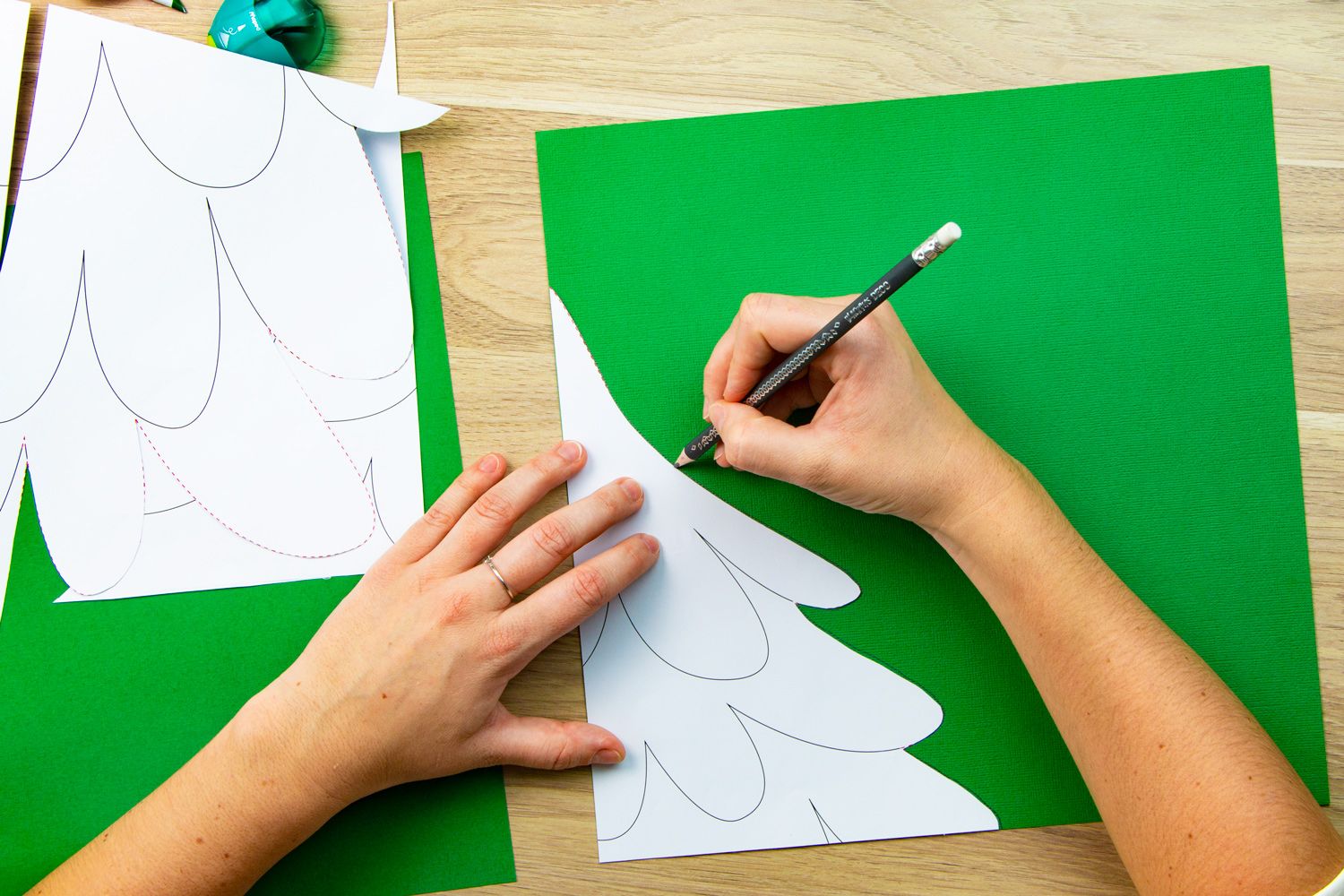 A hand drawing around a Christmas tree template onto green paper