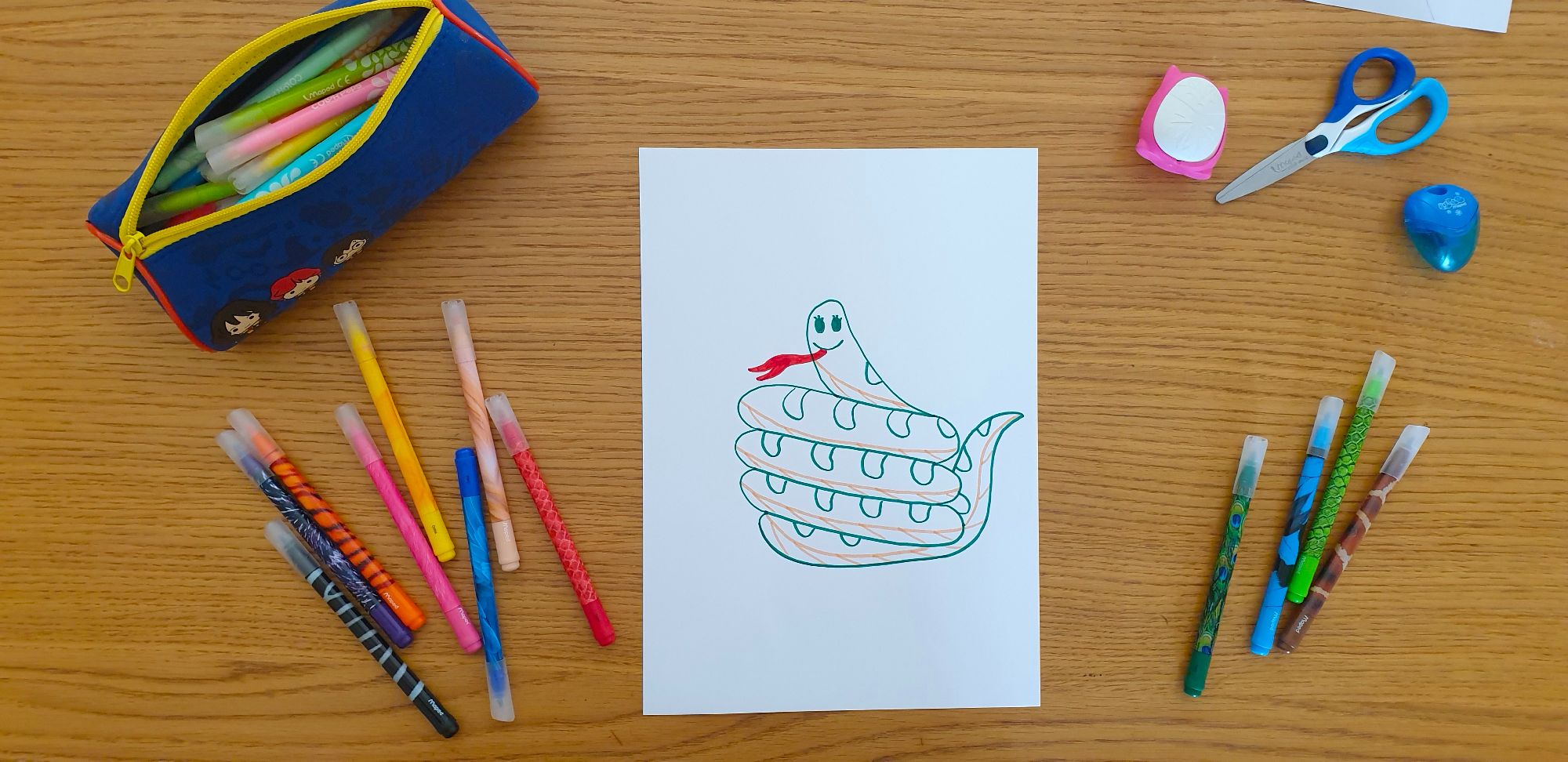 A piece of paper with a drawing of a snake laying on a desk surrounded by stationery