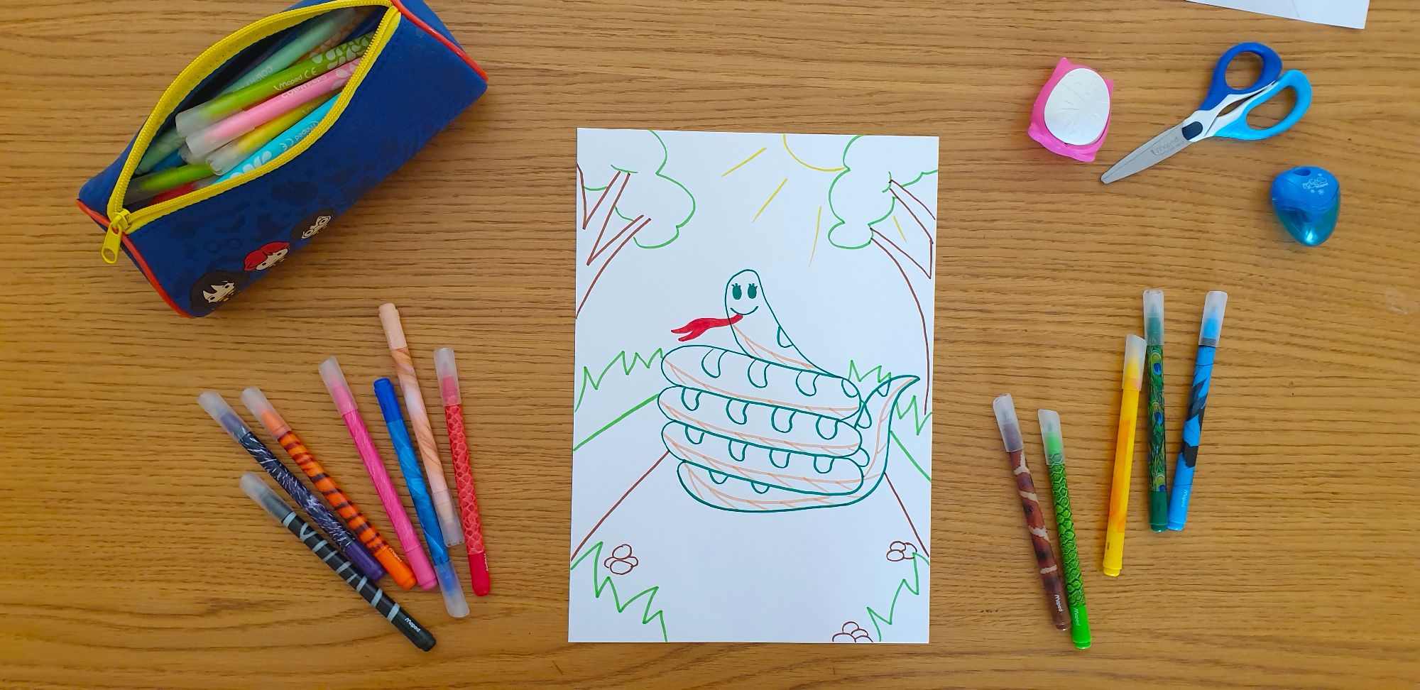 A piece of paper with a drawing of a snake laying on a desk surrounded by stationery