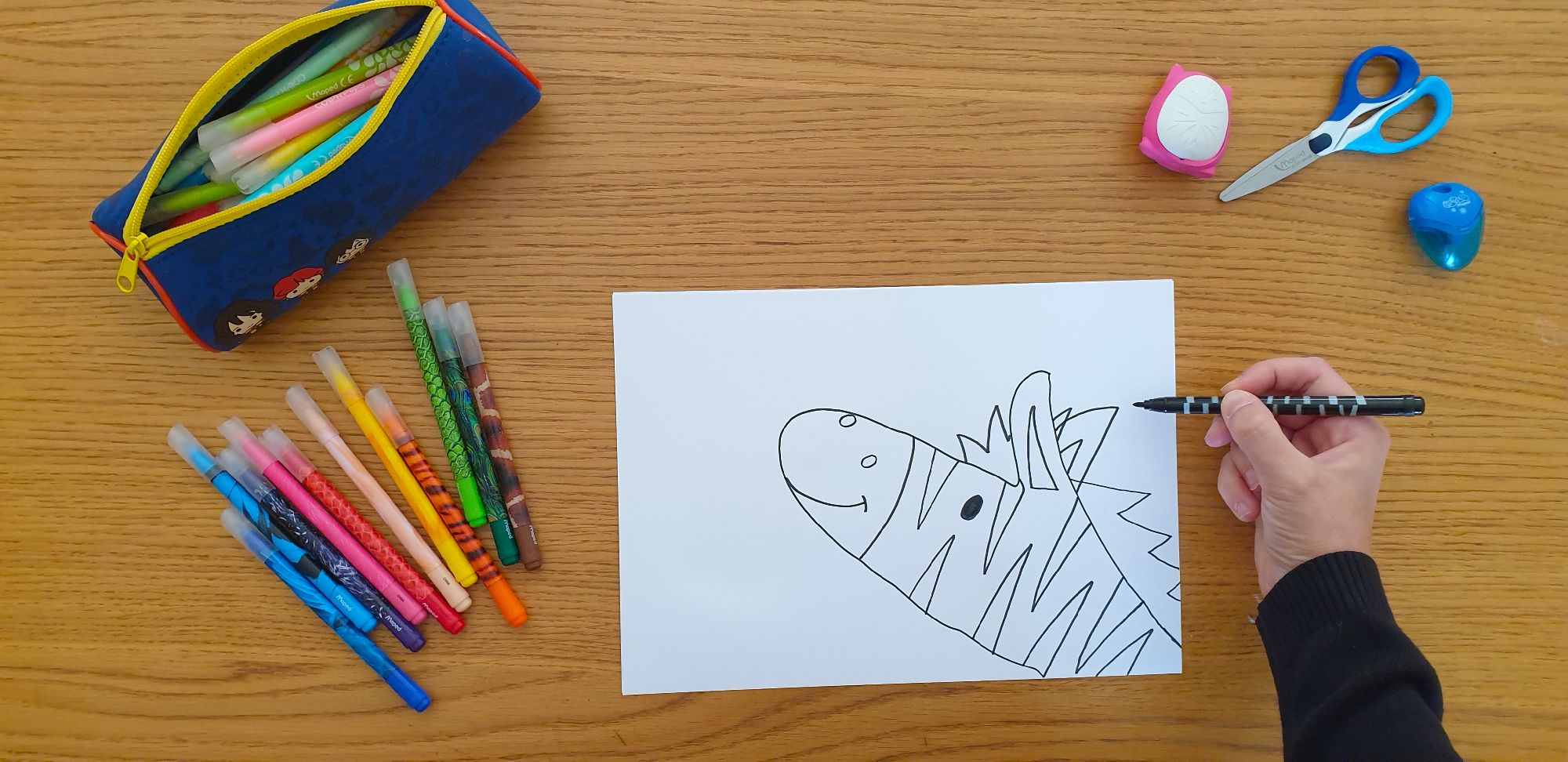 A piece of paper with a drawing of a zebra laying on a desk surrounded by stationery