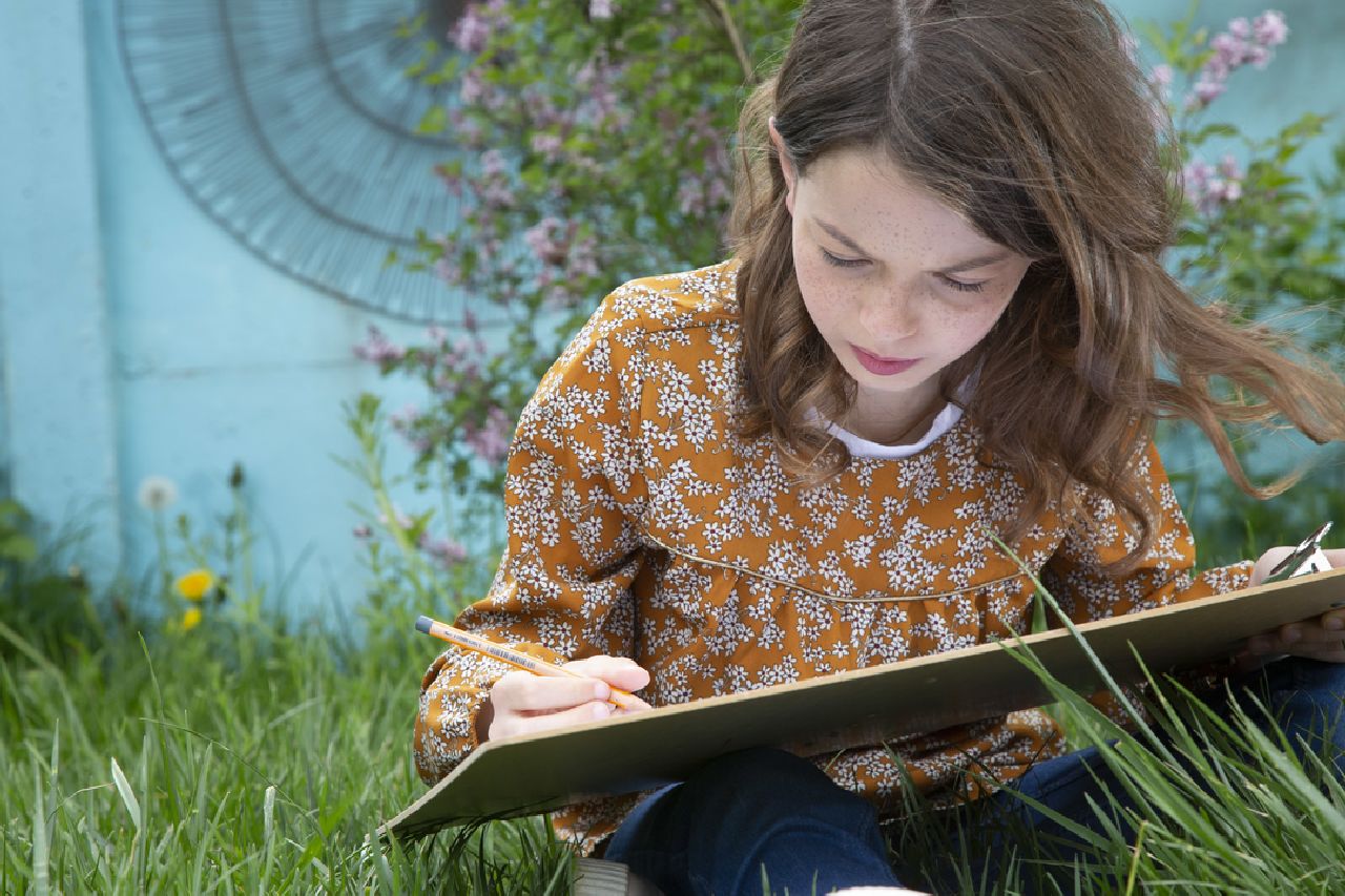 A girl sat on the grass writing in a notebook