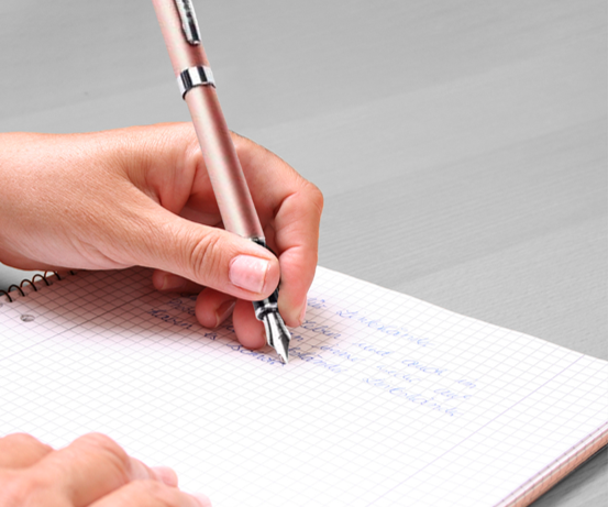 A hand writing in a notebook with a fountain pen