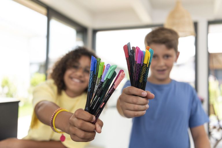 Two children smiling and holding up handfuls fineliners