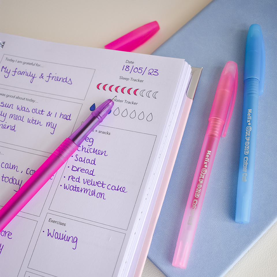 A mental health journal surrounded by purple, pink and blue gel pens.