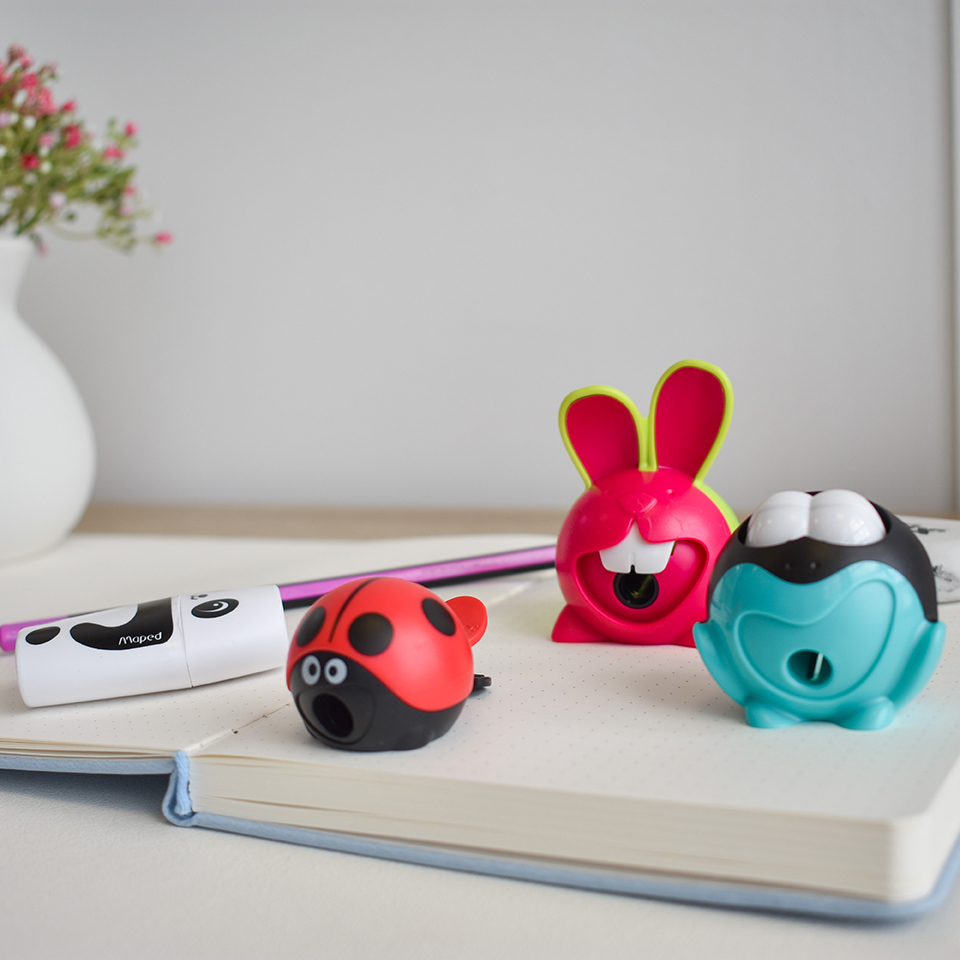A panda, Frog and Bunny pencil sharpener sitting on an open book.