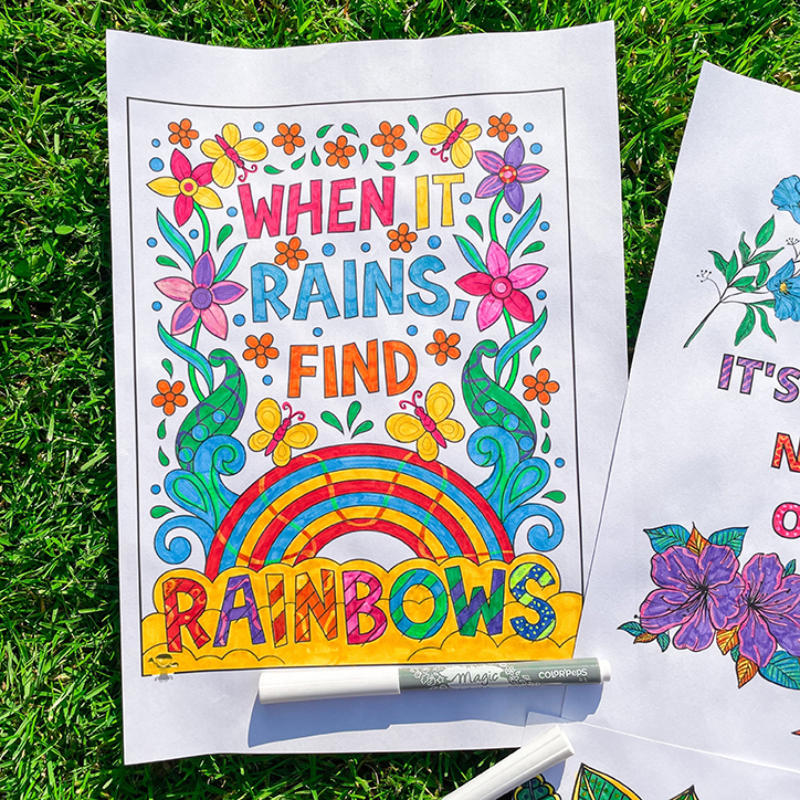 Coloured in A4 that says "When it rains, find rainbows". The paper is lying on green grass.