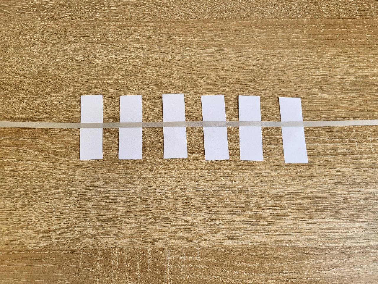 6 strips of paper in a line with a white ribbon lying across the top