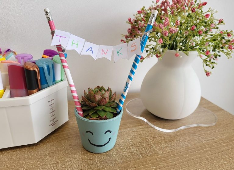 A small plant on a desk with bunting hanging over it spelling thanks
