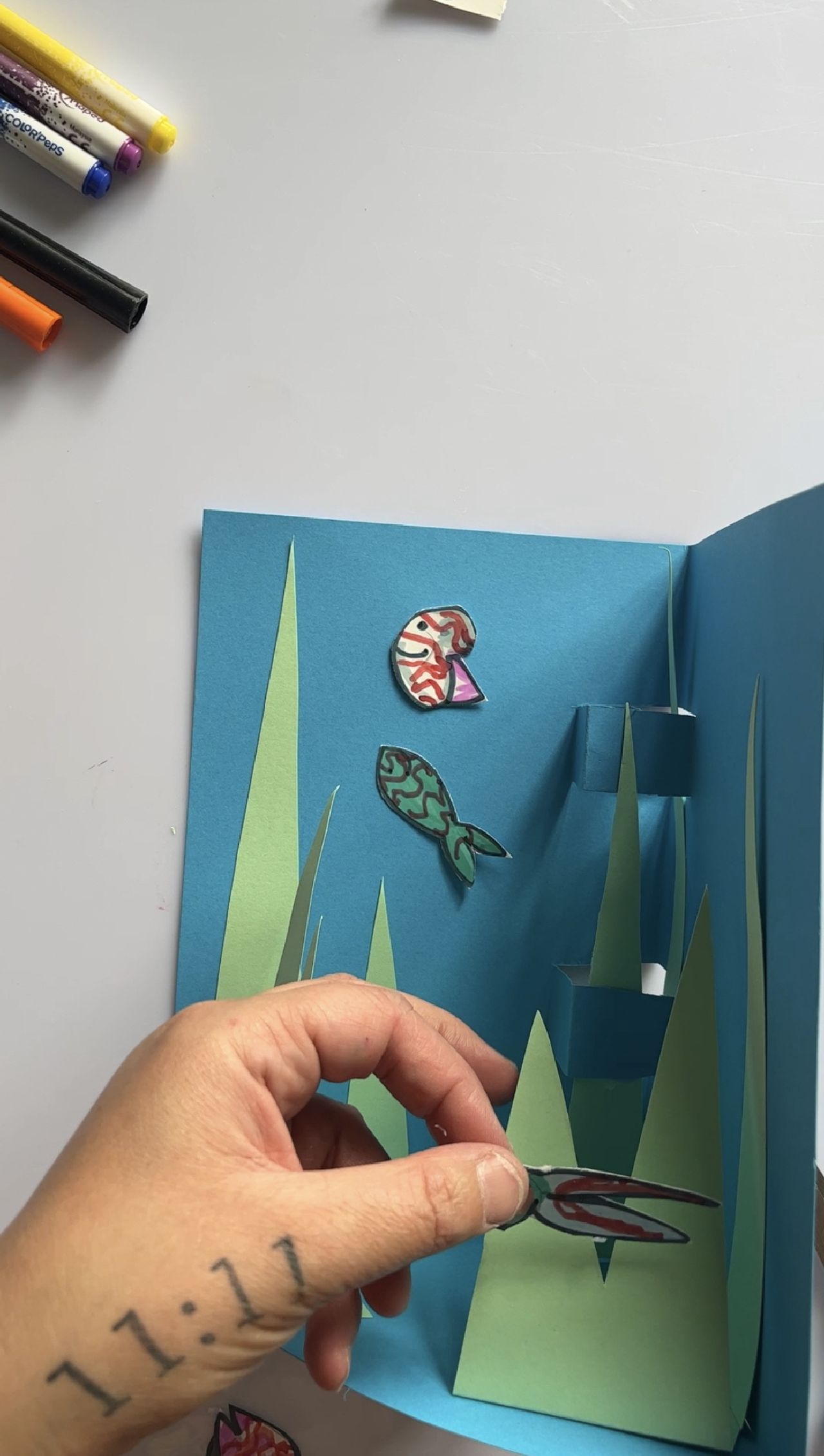 A hand gluing a paper fish onto the 3D aquarium