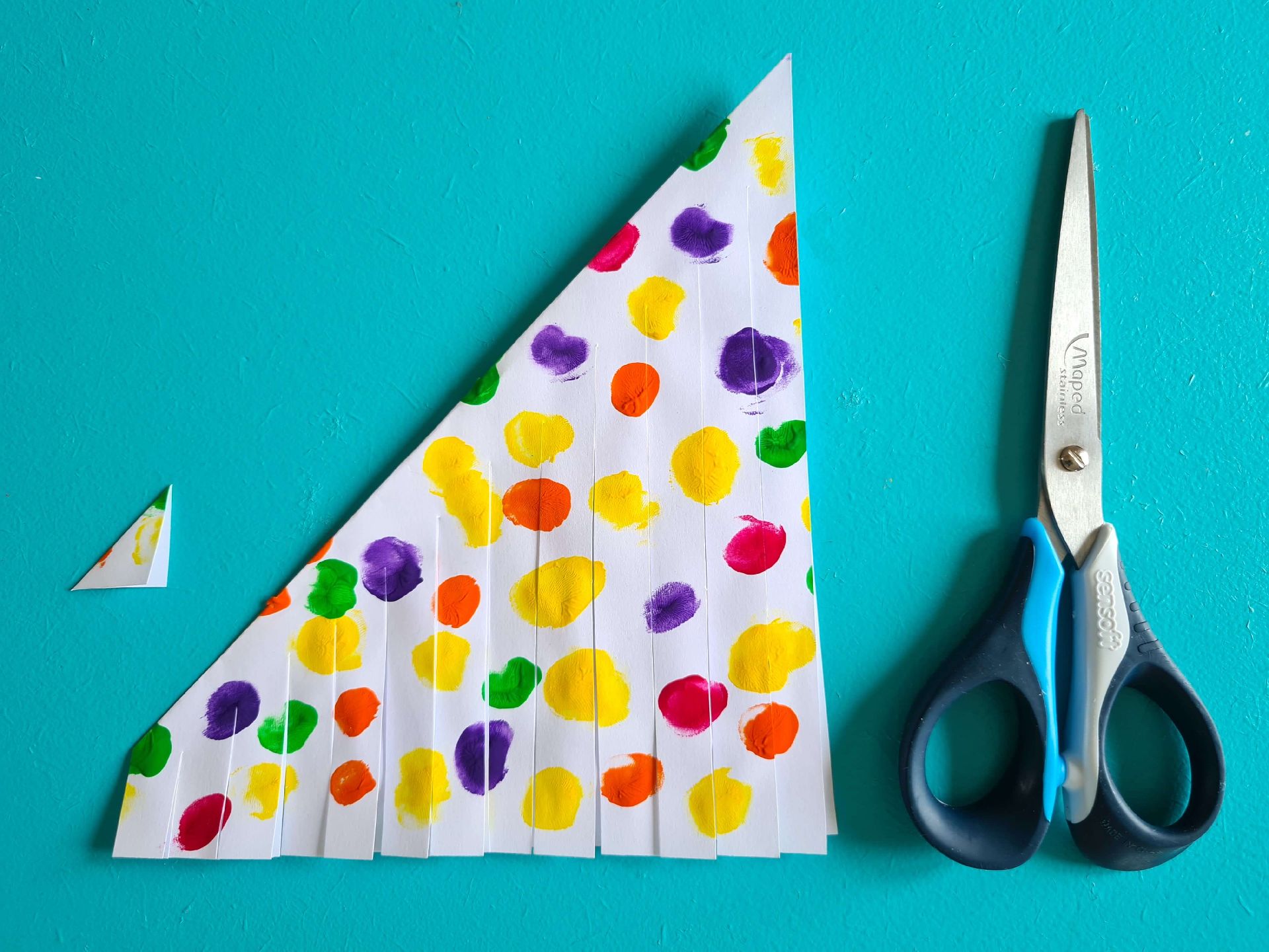 A sheet of paper with coloured dots painted on folded into a triangle with cuts through the paper