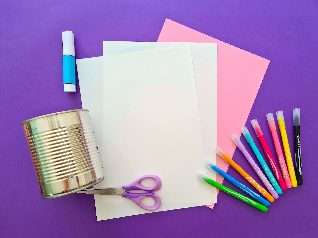 Coloured paper, tin can, felts and scissors laying on a purple background