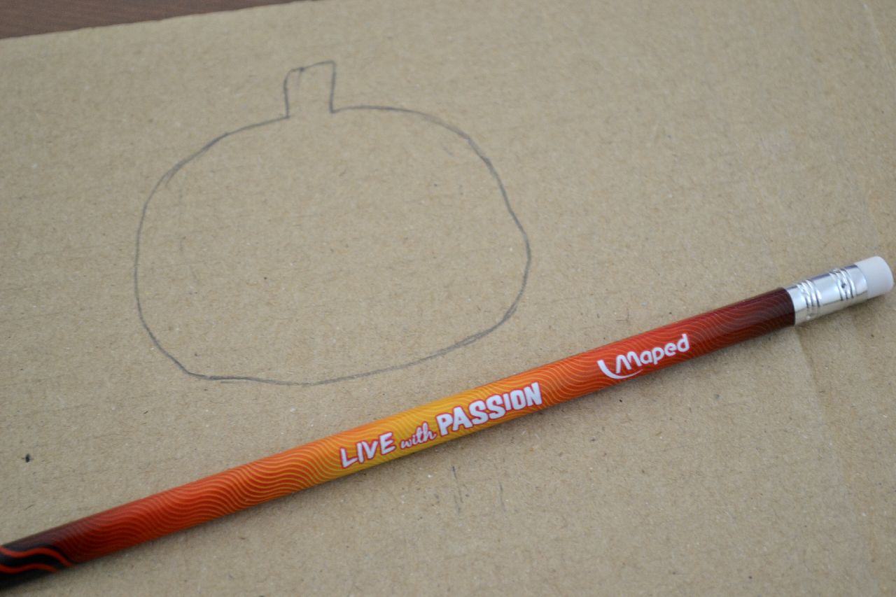 A pencil laying next to a hand drawn pumpkin on a piece of card