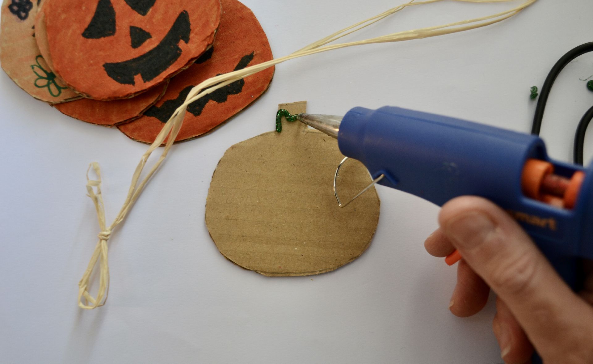 a glue gun applying glue to the back of the cardboard pumpkin